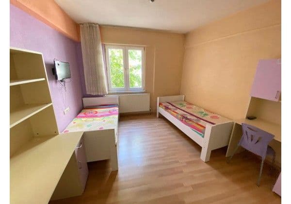 İki kişilik yurt odası, iki tek yatak, çalışma masaları ve duvara monte TV