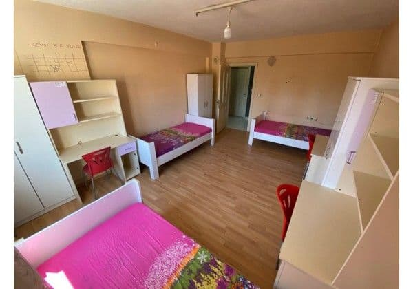 Üç kişilik yurt odası, üç tek yatak, gardıroplar ve çalışma masaları